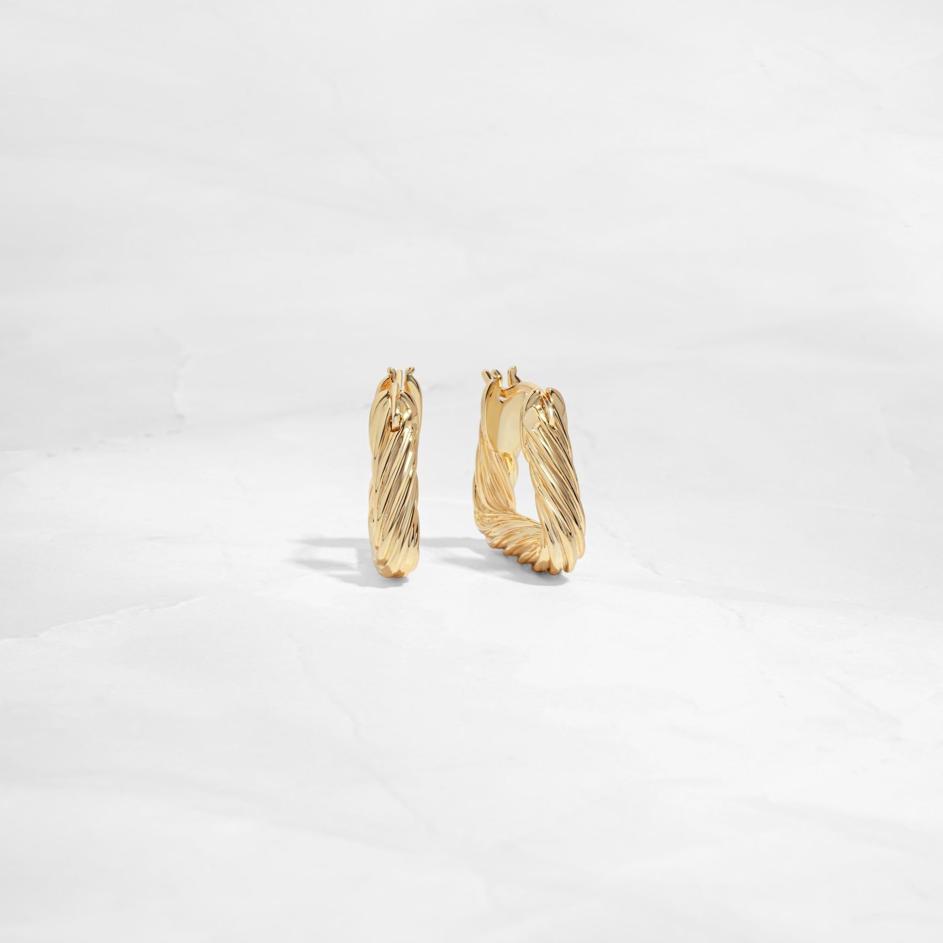 Side and front profile of chunky gold hoop earrings with a geometric design.