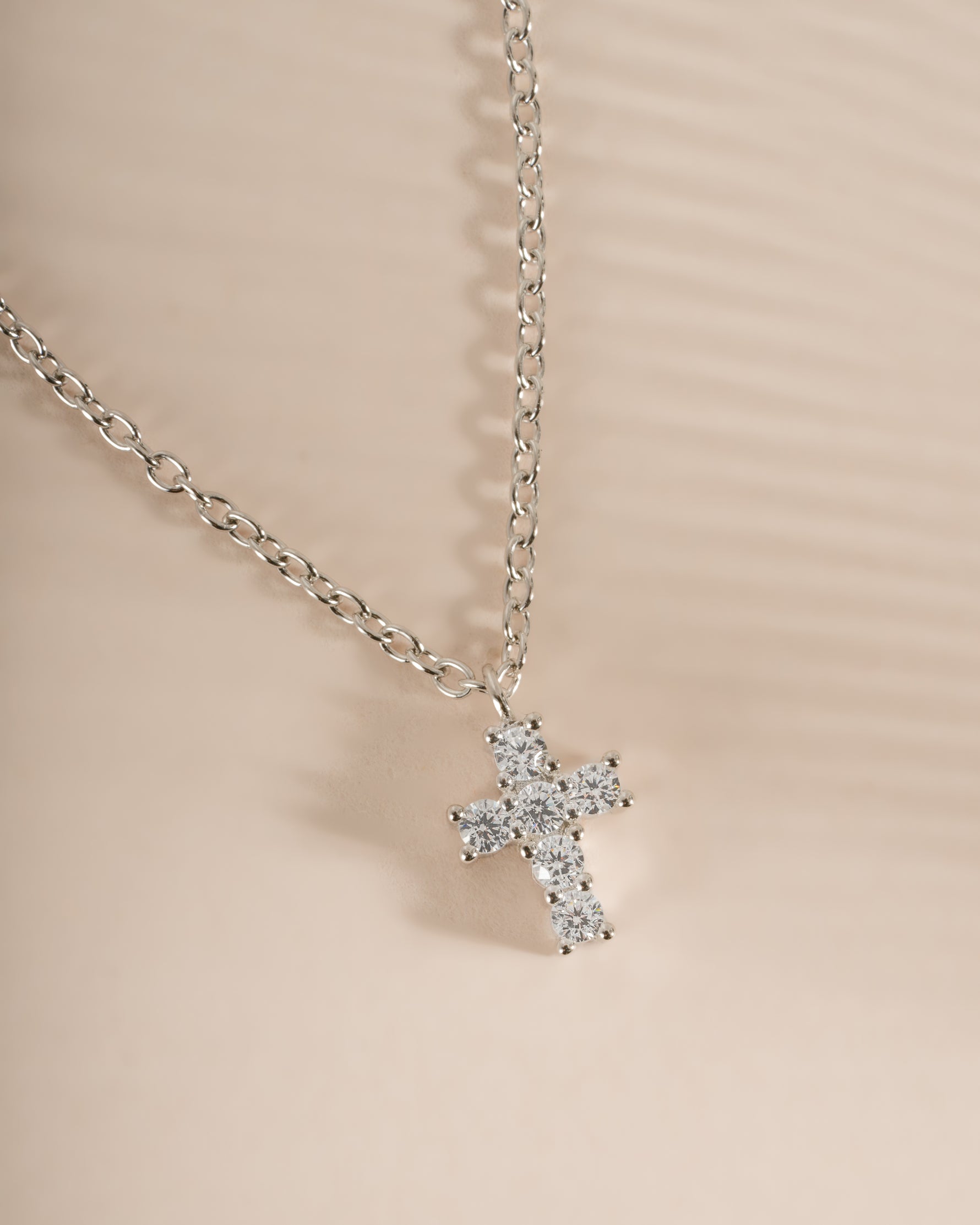 Close-up of a sterling silver Tiny Cross Necklace pendant from Sami Jewels, showing the delicate cross design on a chain.