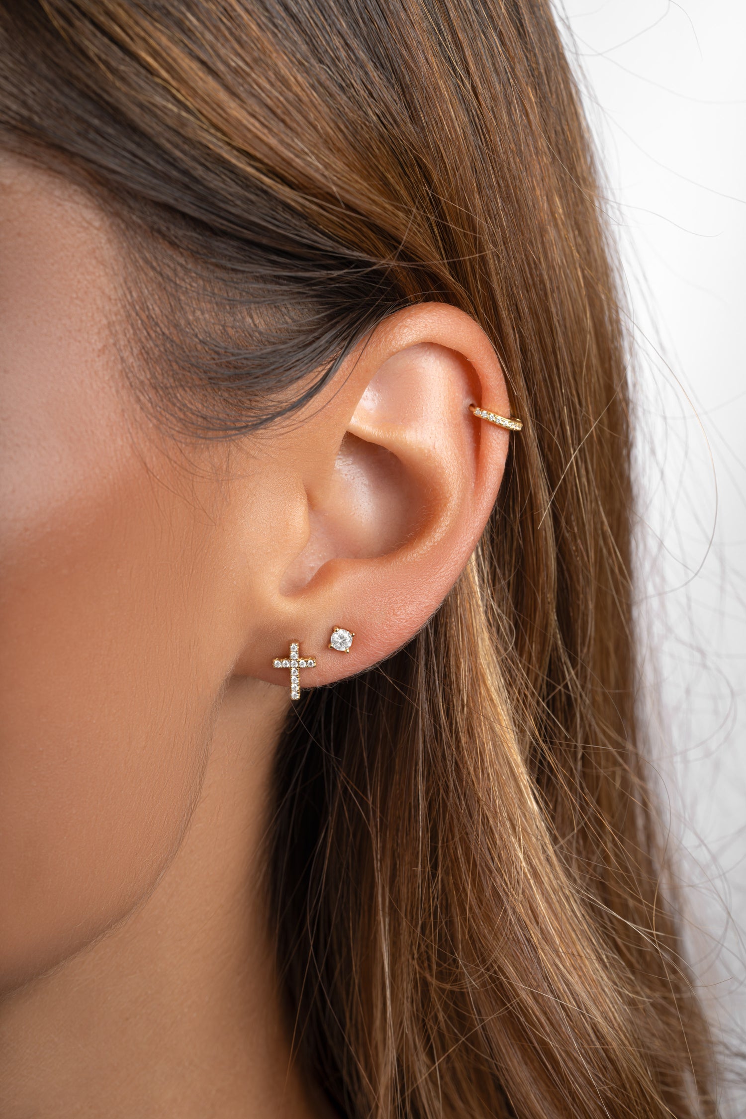 Gold tiny cross stud earrings from Sami Jewels, close-up of small cross-shaped earrings worn on ears.