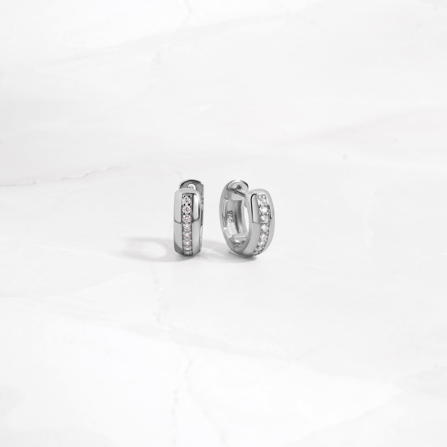 close up of minimalist silver diamond huggies showing intricate detailing. 