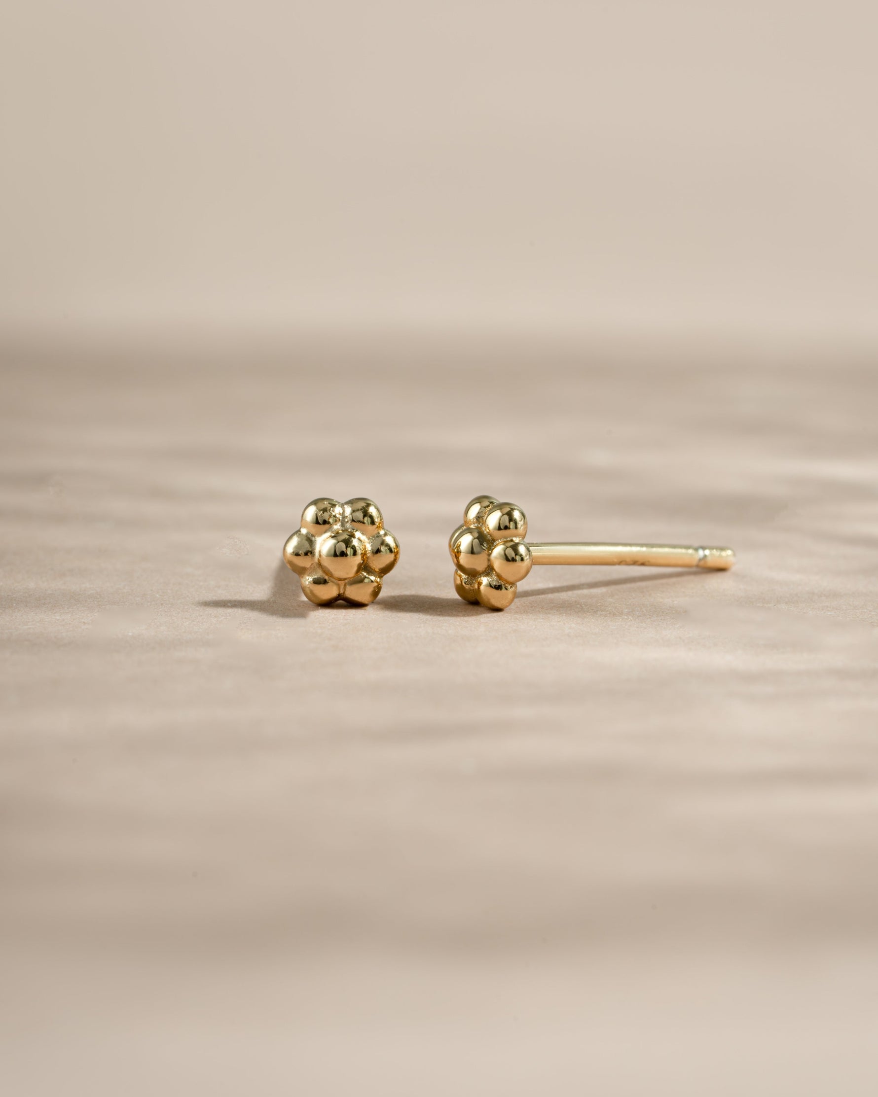 Gold tiny flower stud earrings from Sami Jewels featuring delicate petal design, shown from an angled view.