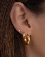tube hoop earrings in gold on models ear paired with gold earrings 
