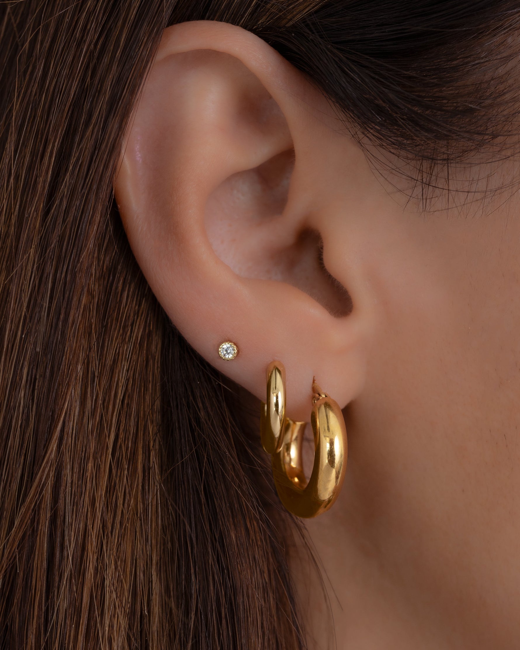 tube hoop earrings in gold on models ear paired with gold earrings 
