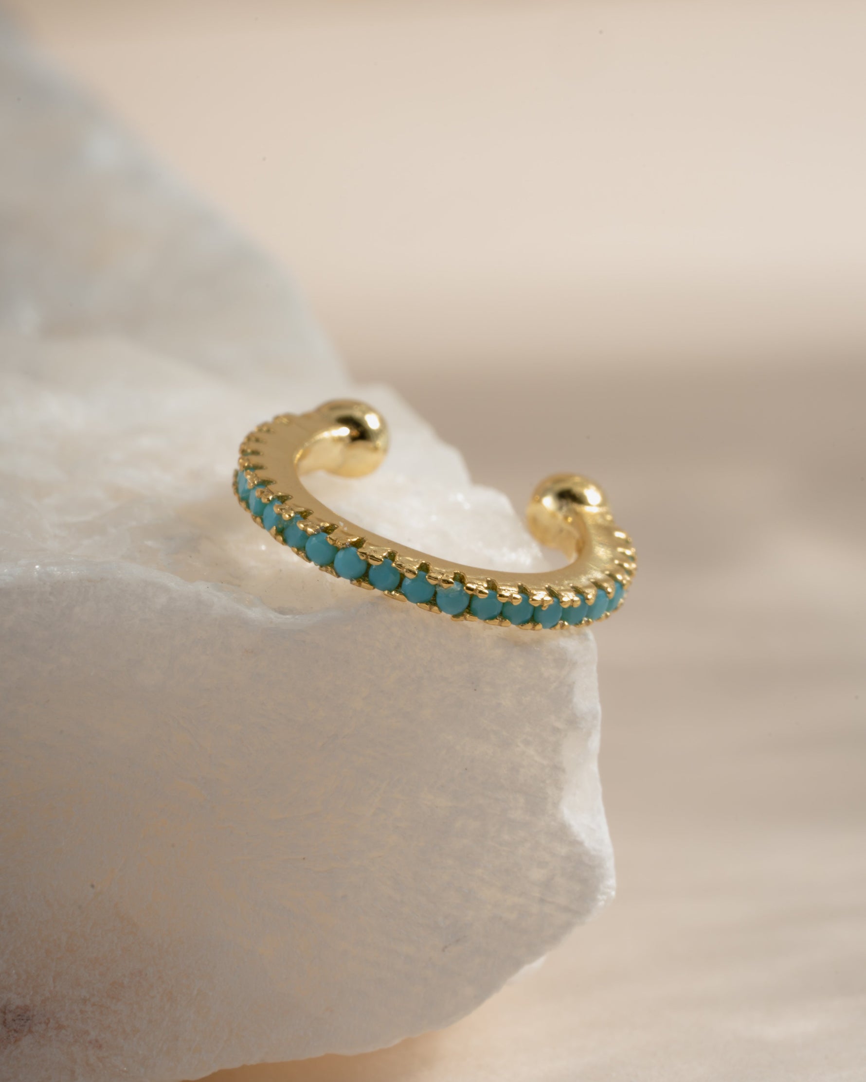Close-up of a gold Sami Jewels turquoise ear cuff showing intricate design and vibrant turquoise stone detail.