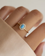 Sami Jewels Layla turquoise oval halo ring on a model's finger, featuring a gold band and a vibrant turquoise gemstone.
