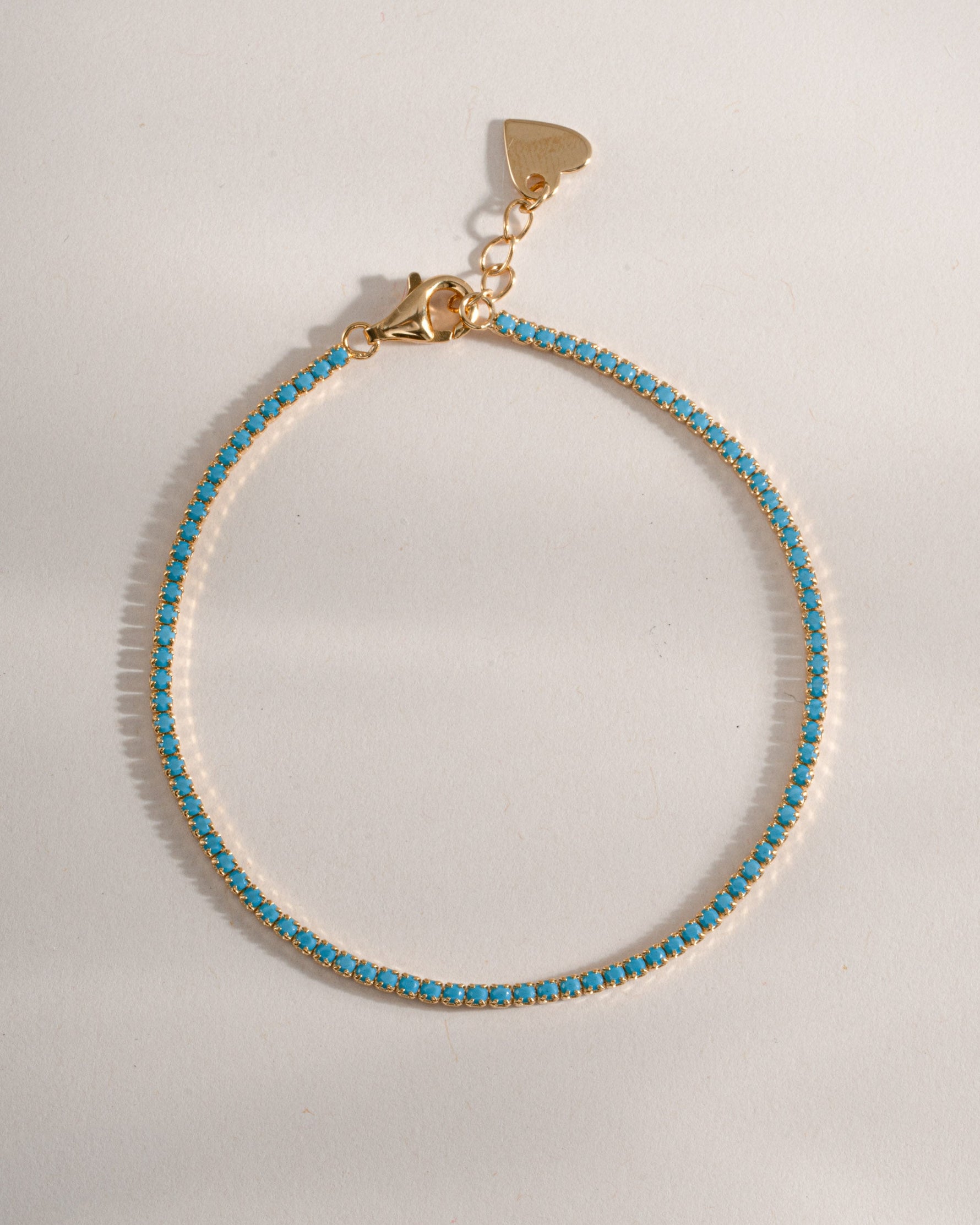 Close-up of Sami Jewels turquoise tennis bracelet showing vibrant turquoise stones and gold setting on a white background.