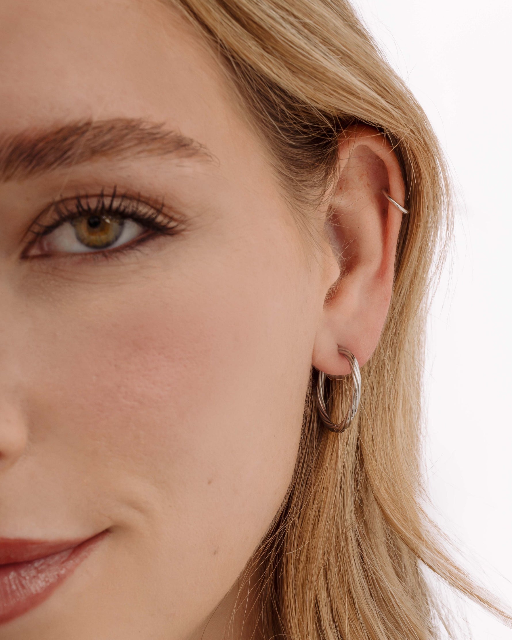 Silver stainless steel SS Twisted Hoops earrings with a sleek twisted design, worn by a model.