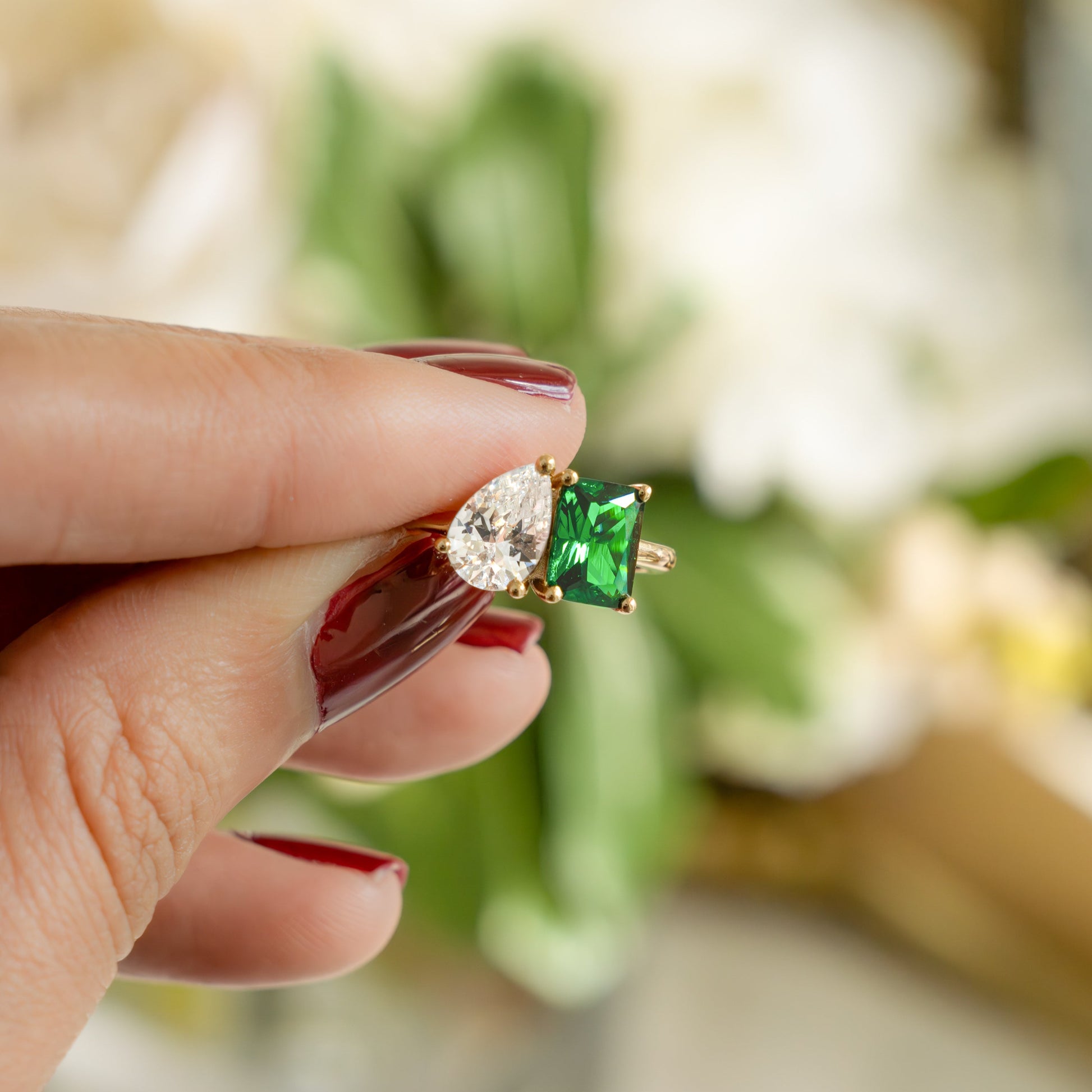 a model holding a toi et moi promise ring that is made with an emerald cut emerald stone set against a cubic zirconia pear shaped stone