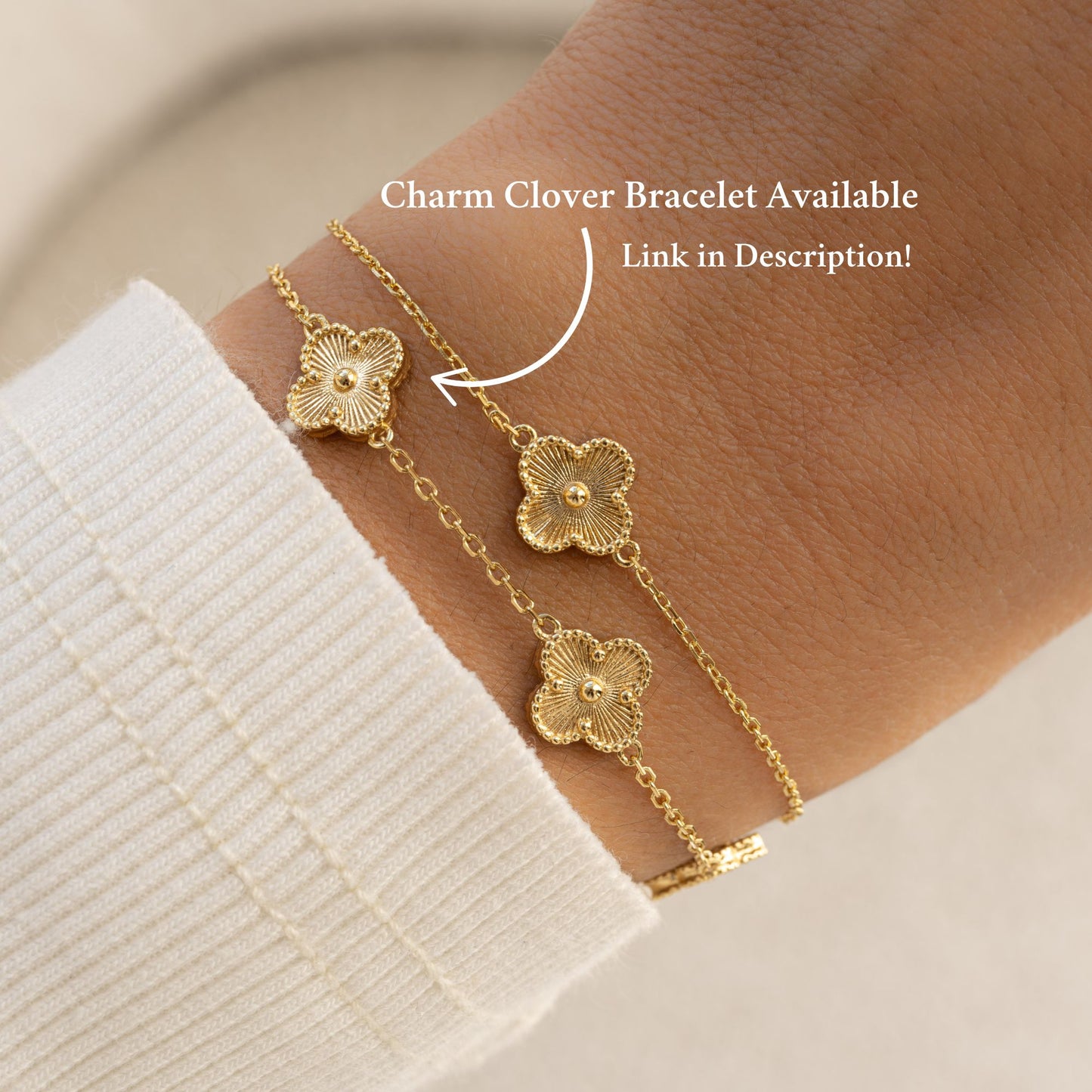 A model wearing two bracelets, one of a four leaf clover bracelet in gold with a charm bracelet with five four clover leaf charms.