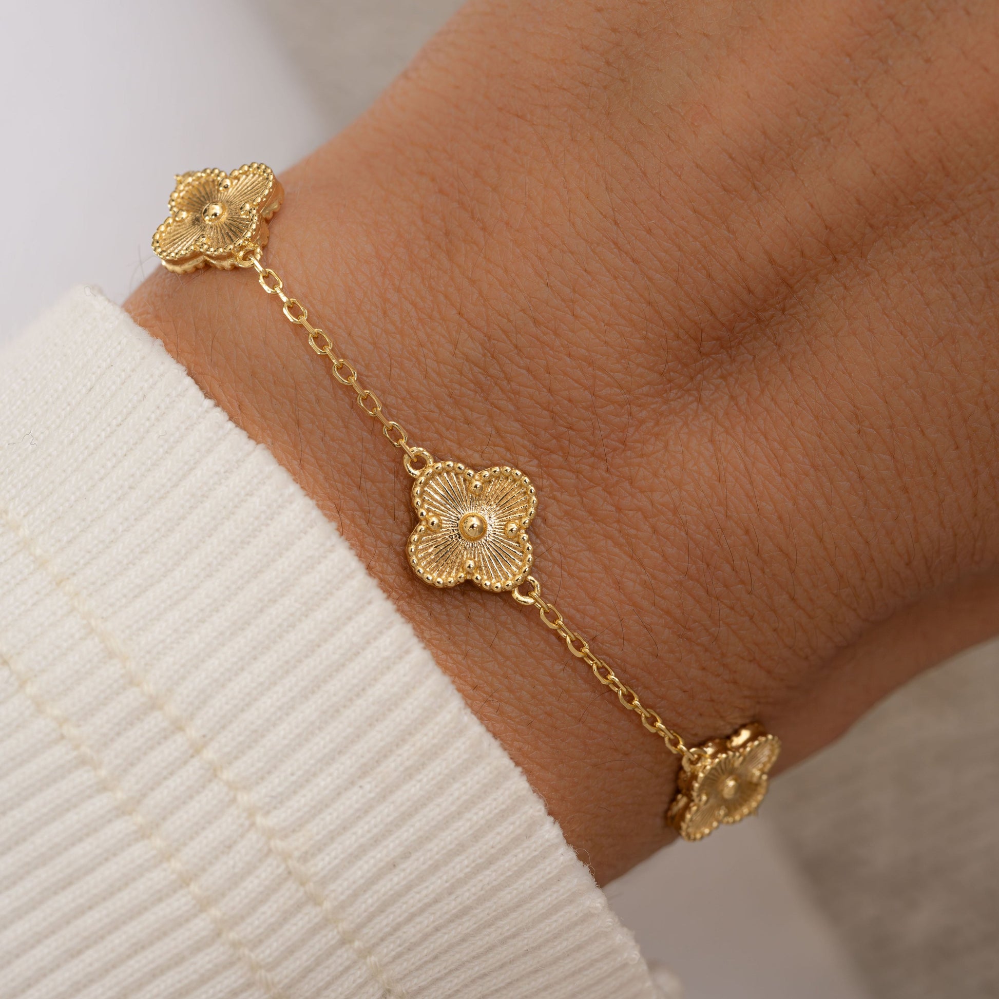 Model wearing a dainty charm bracelet with  a gold four leaf clover charm