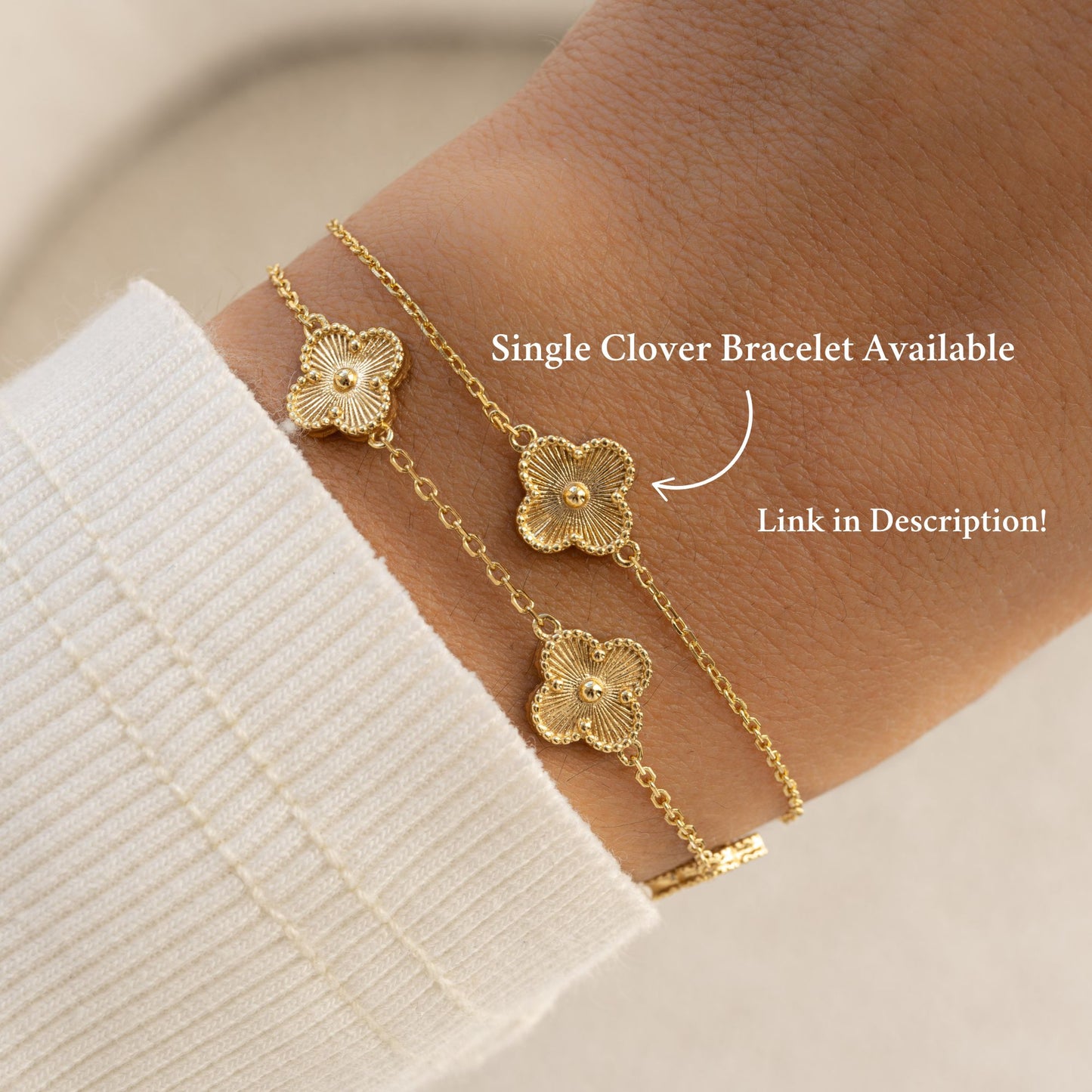 Close-up of a single clover charm bracelet paired with a five-charm clover bracelet that can be stacked together, worn by the model.