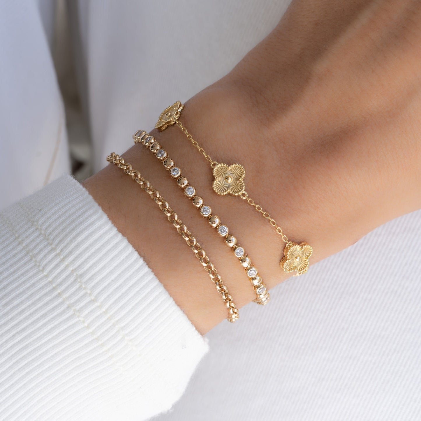 Model wearing a four leaf clover bracelet as part of a layered wrist stack with chain bracelet and diamond tennis bracelet.