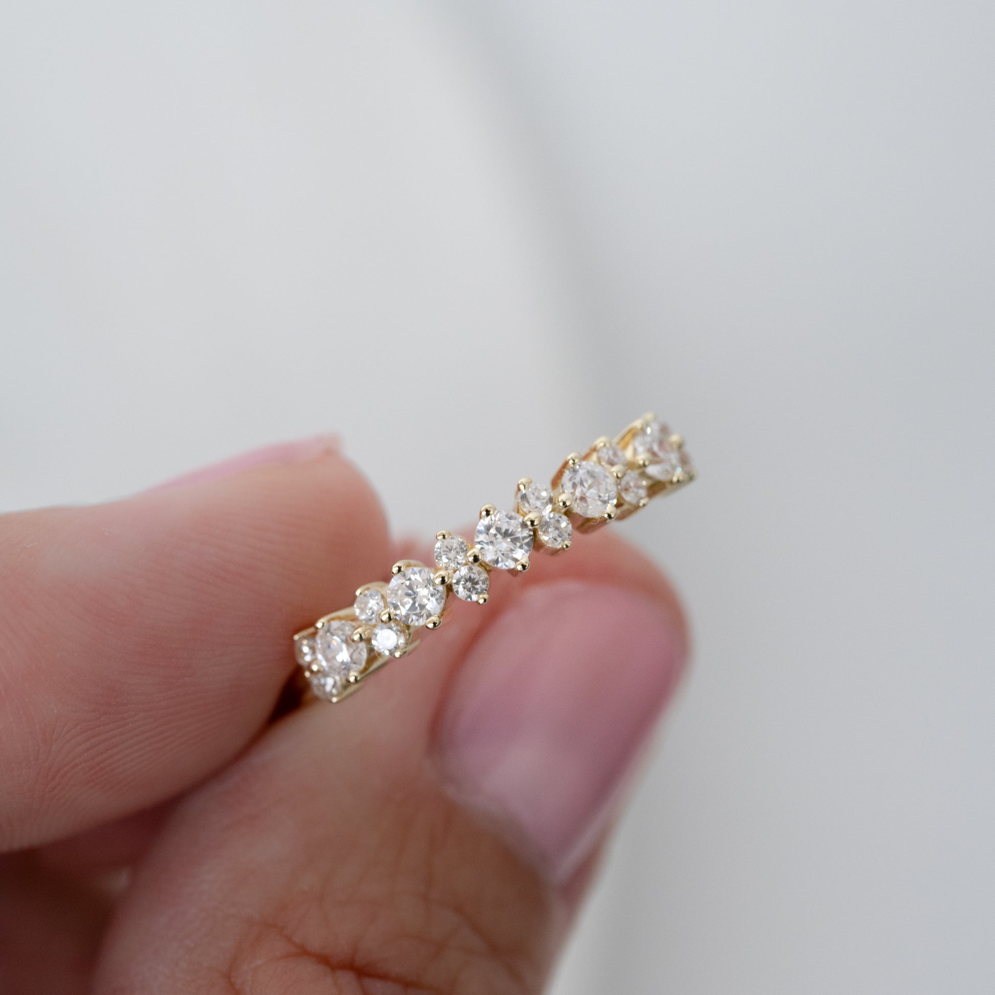 a model holding a dainty gold ring with cubic zirconia stones on it, the ring is minimalist and dainty