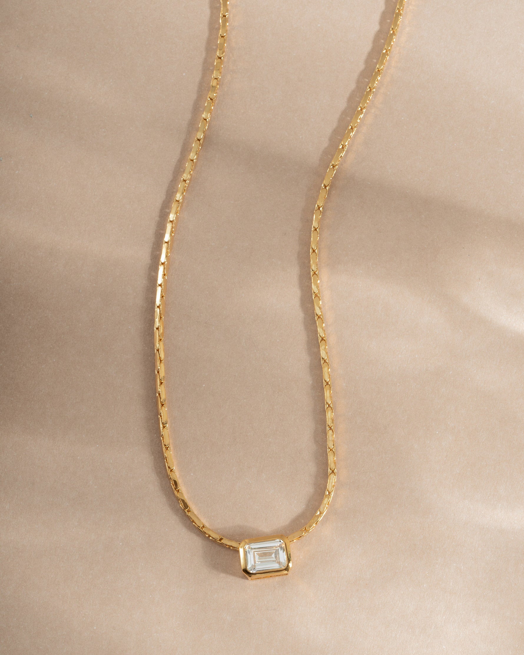 Gold flatlay of Sami Jewels white CZ baguette bezel statement necklace showcasing sparkling rectangular stones.
