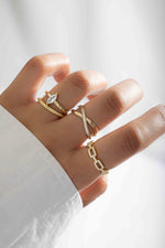 Gold X-shaped statement ring from Sami Jewels, featuring a bold design on a model's hand.