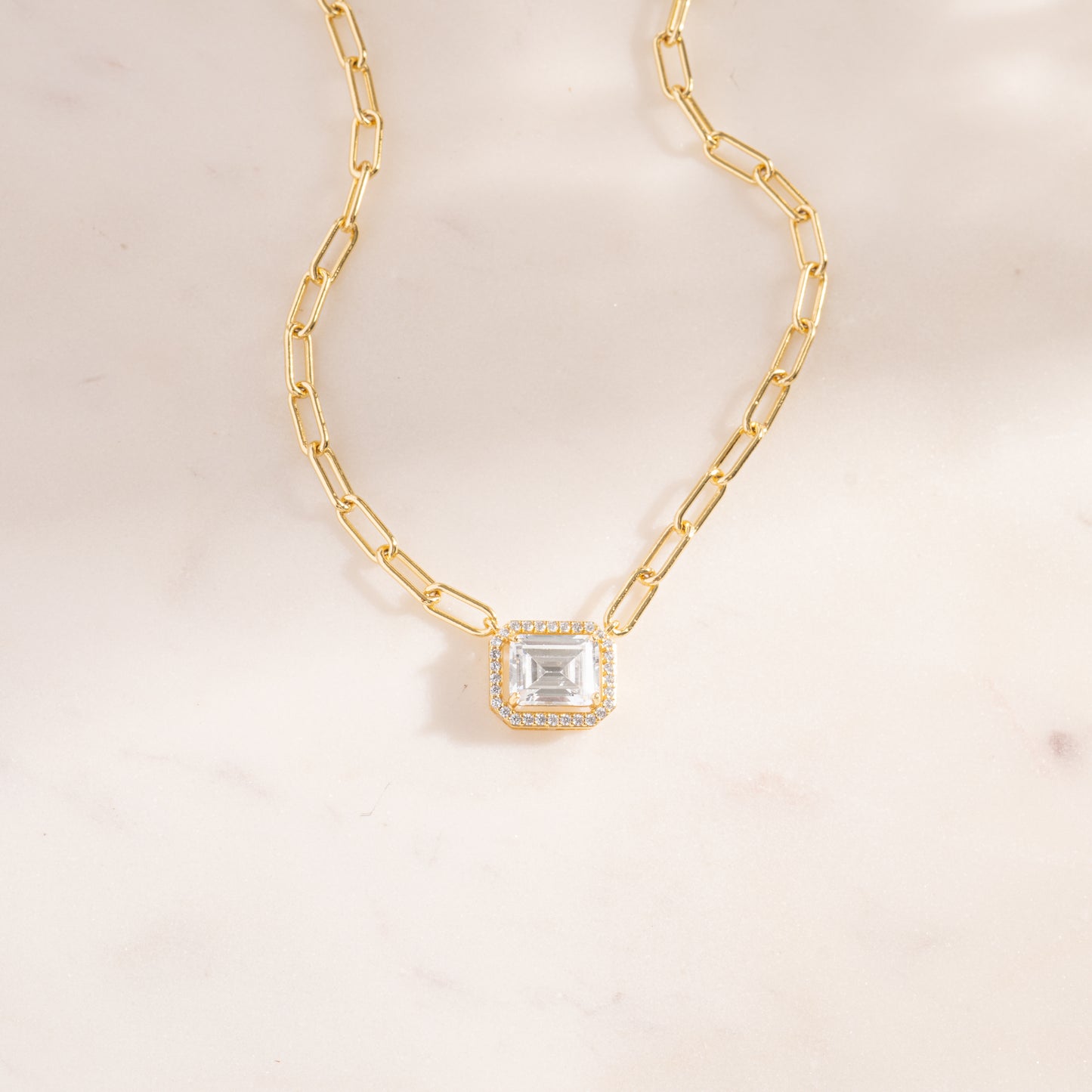 a gold necklace with a square cut stone on a chain