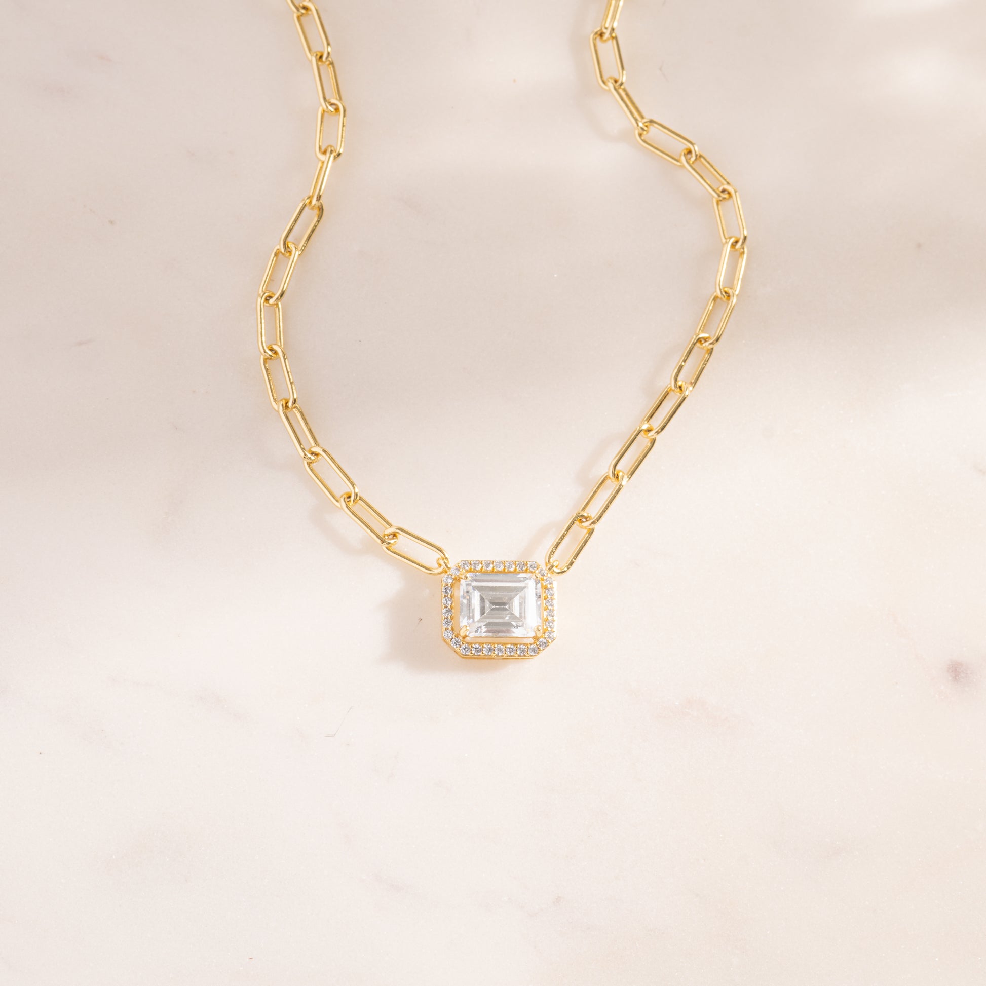 a gold necklace with a square cut stone on a chain