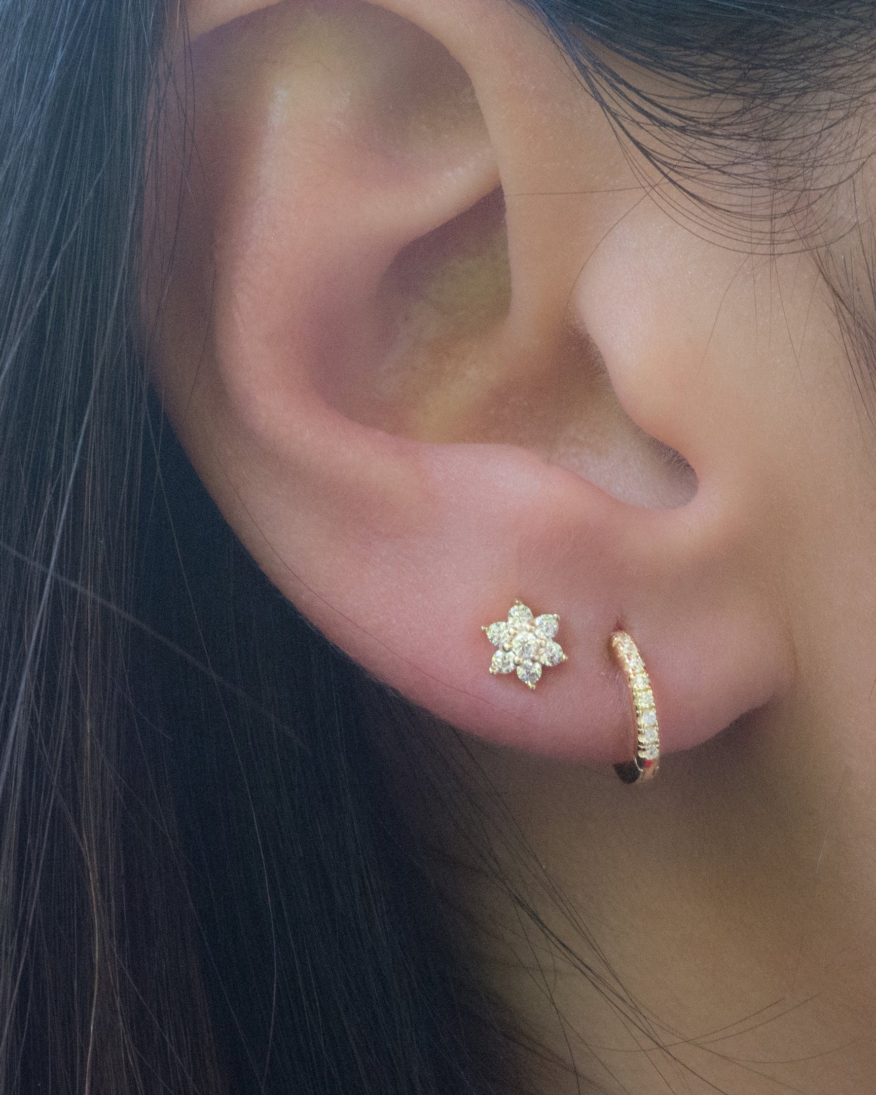 Model wearing gold cz studded huggie earring and diamond flower stud earrings in gold. 