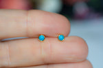 Model holding dainty gold turquoise round stud earrings. 