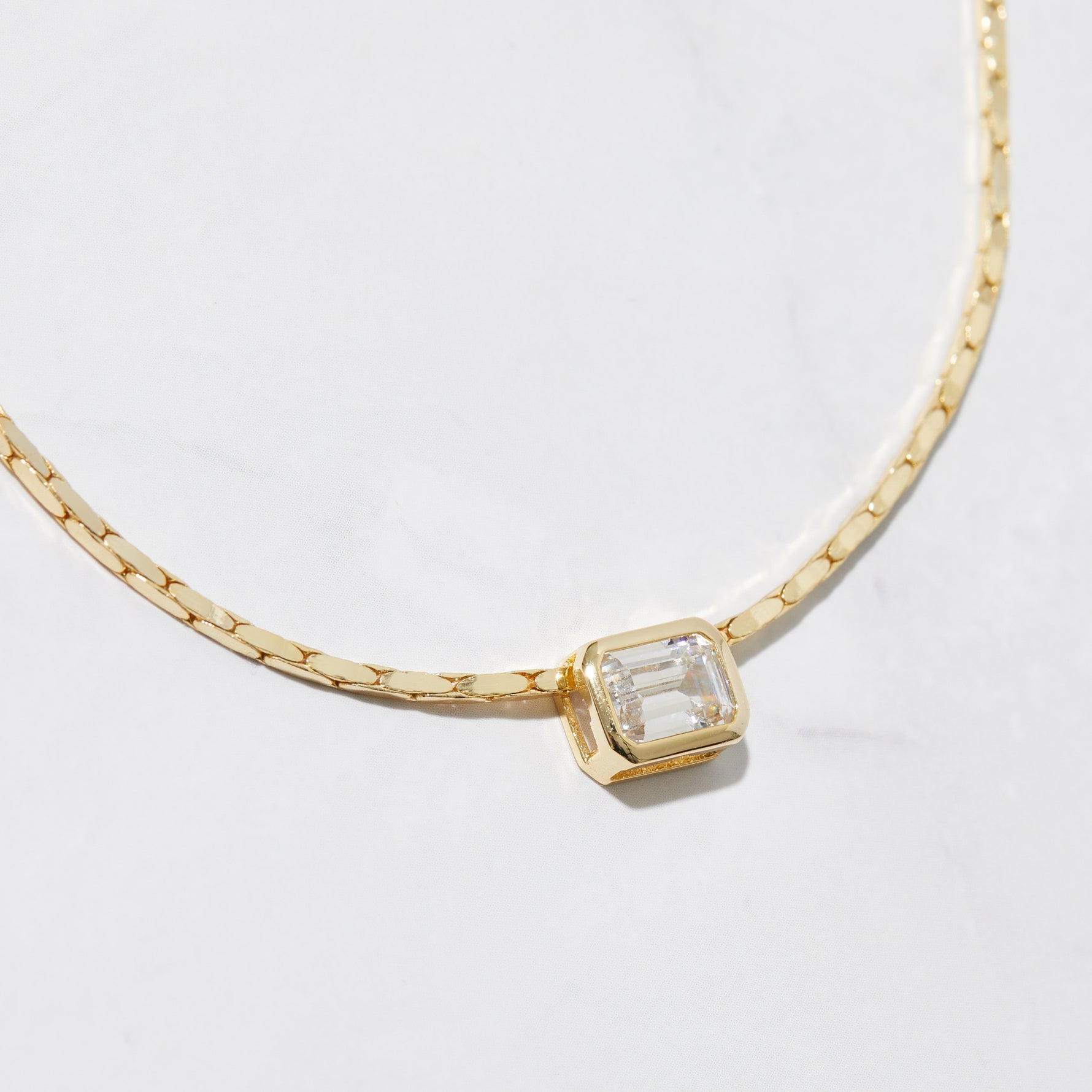 Close-up of gold baguette bezel pendant necklace on white background