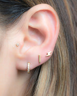 Model wearing lightning bolt stud, plain bar stud, and cz huggies. 