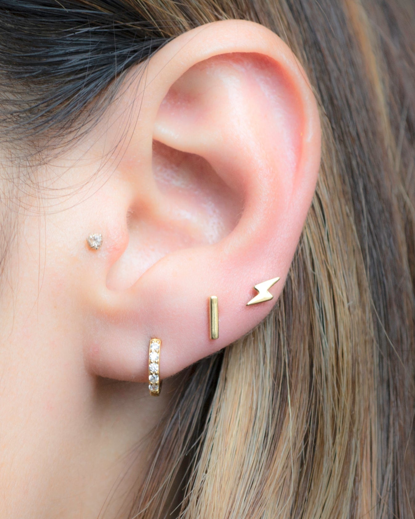 Model wearing lightning bolt stud, plain bar stud, and cz huggies. 