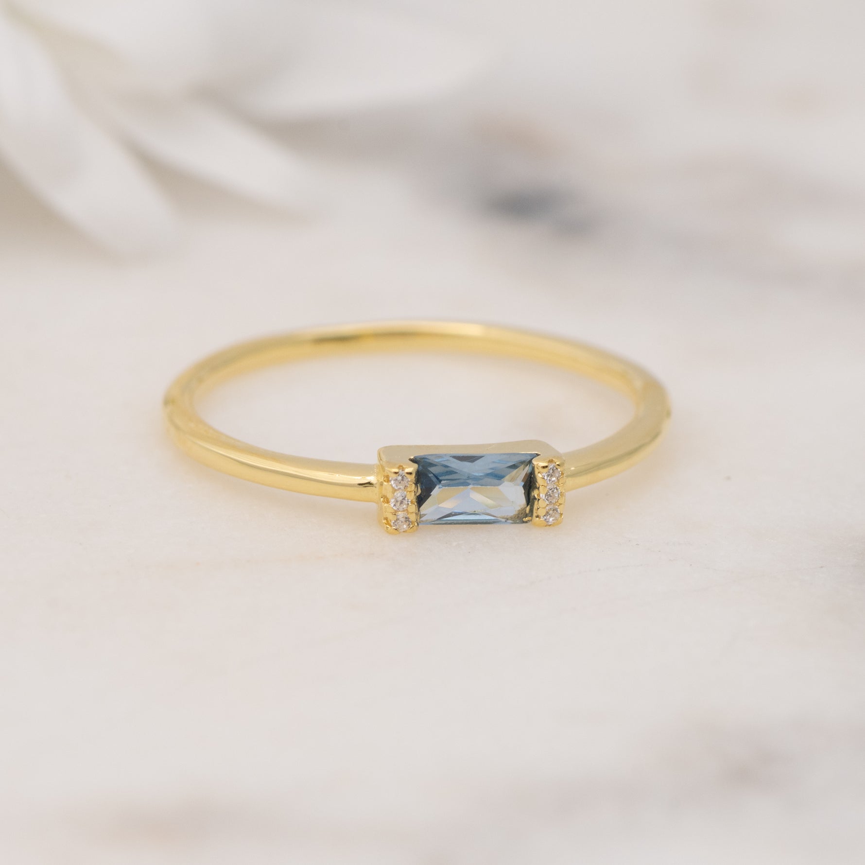 Closeup image of dainty gold aquamarine baguette stone ring on marble background.