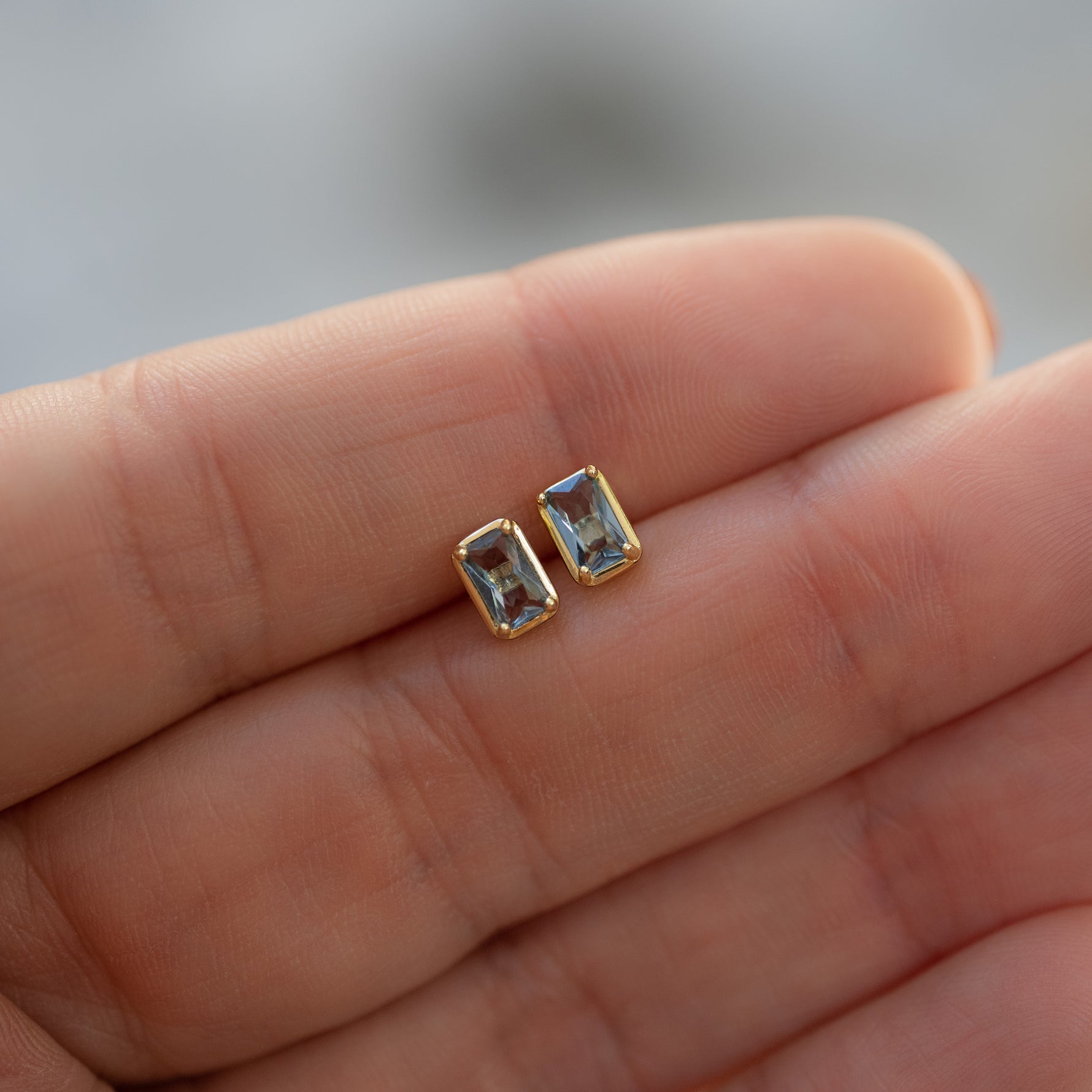 Closeup image of dainty gold aquamarine baguette stud earrings. 