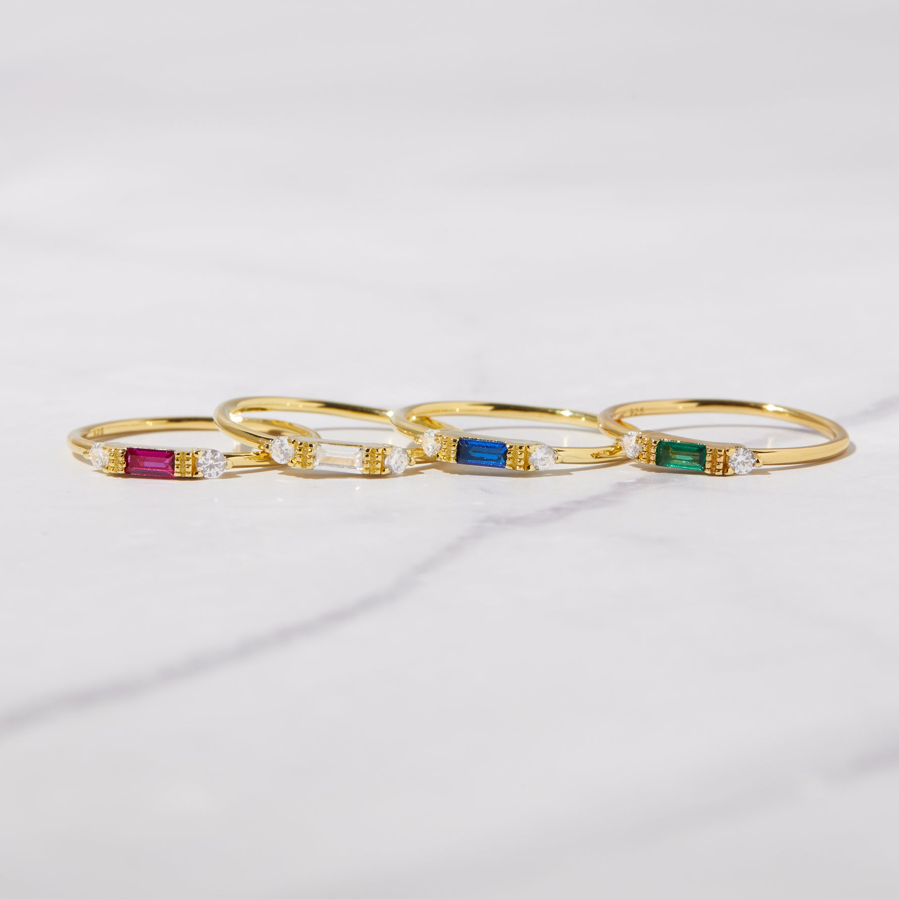 Dainty birthstone rings in gold featuring ruby, diamond, sapphire, and emerald stones. 