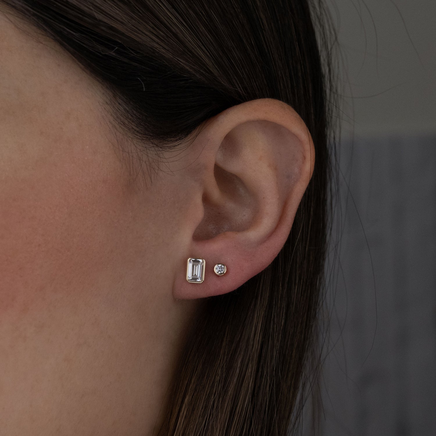 Model wearing classic gold cz diamond stud earrings including an emerald cut stud and a round bezel stud.