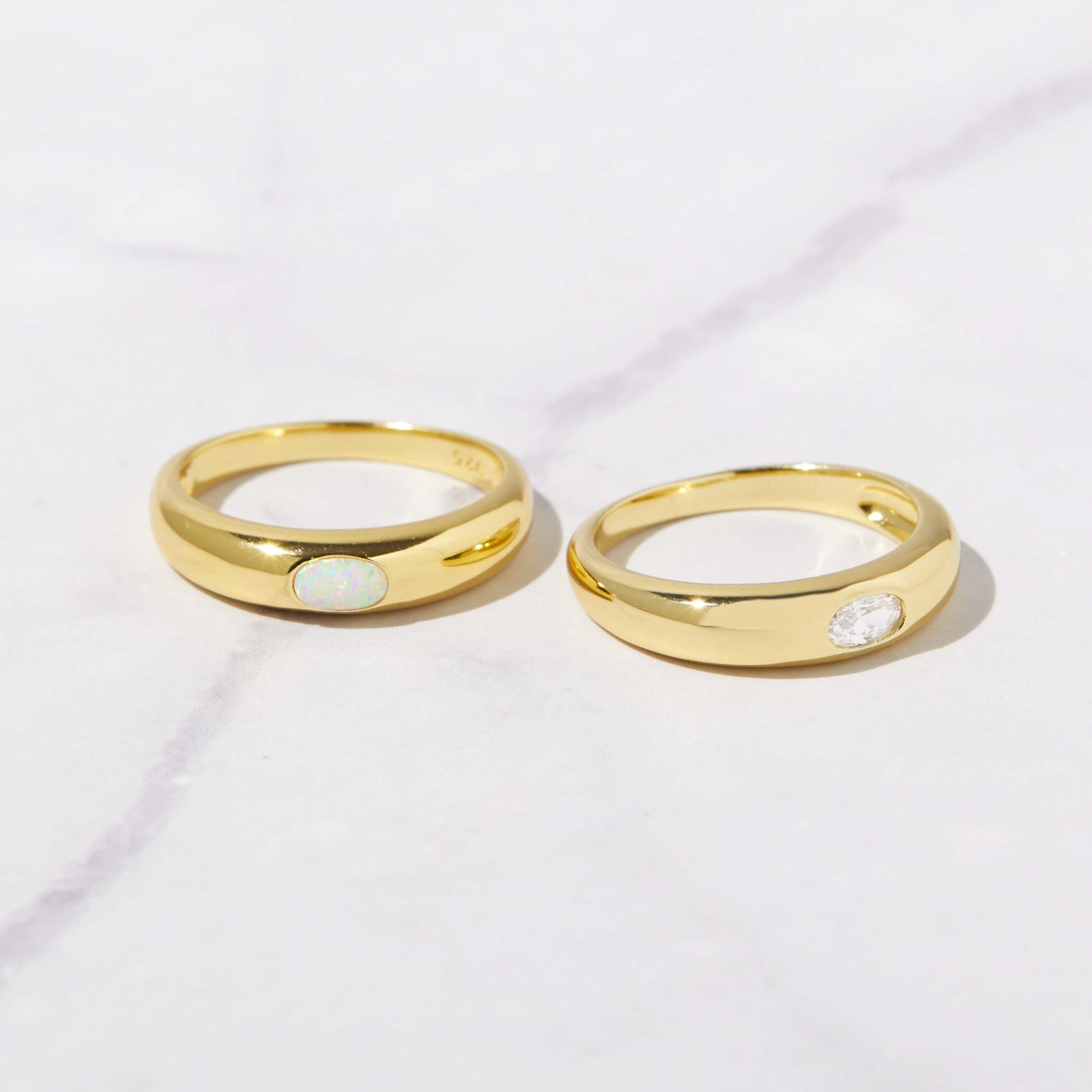 Opal and CZ oval bezeled dome rings in gold on marble background. 