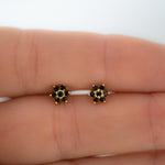 Upclose shot of black floral design stud earrings in gold. 