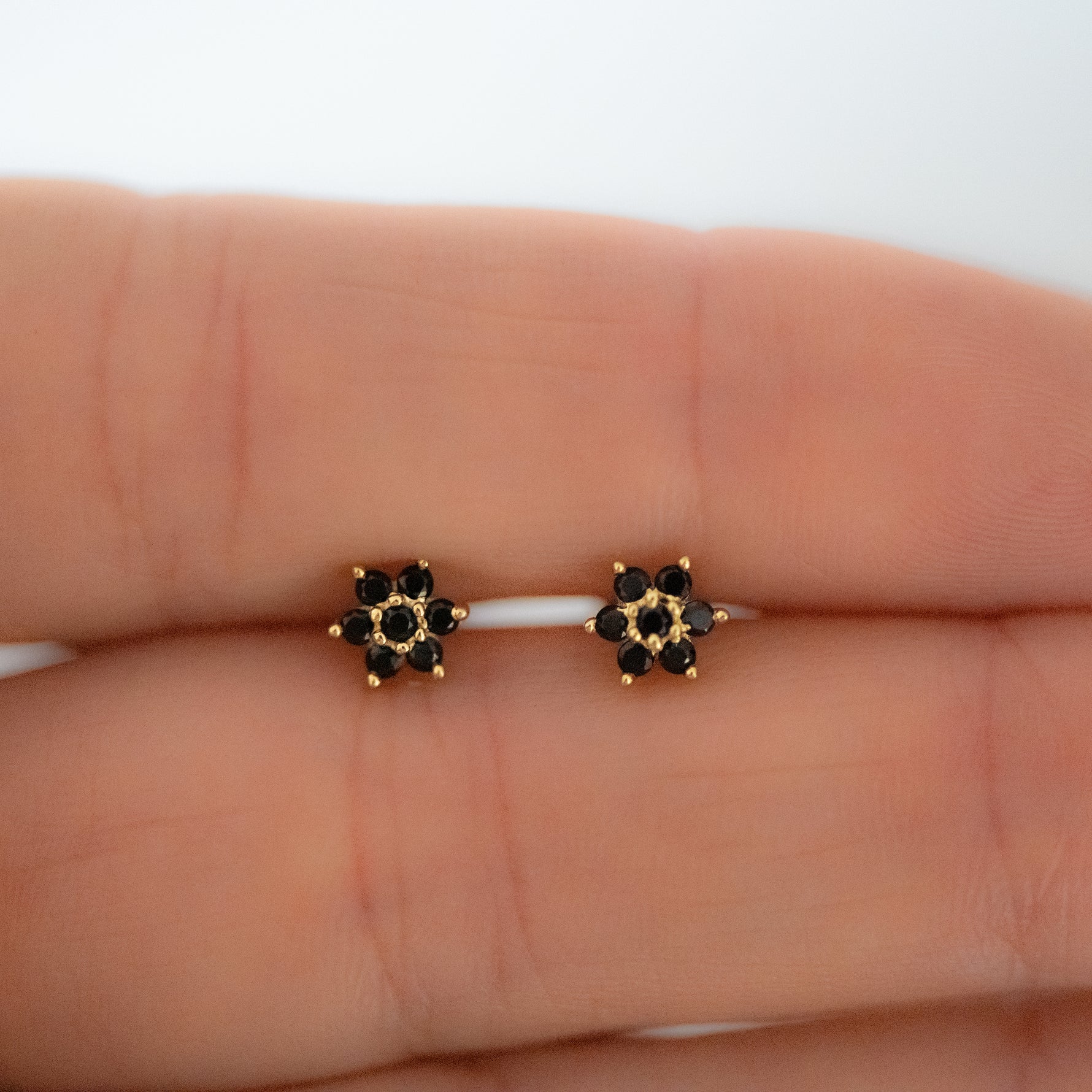 Upclose shot of black floral design stud earrings in gold. 