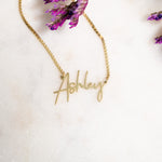 Flat lay wearing gold script custom name necklace with box chain