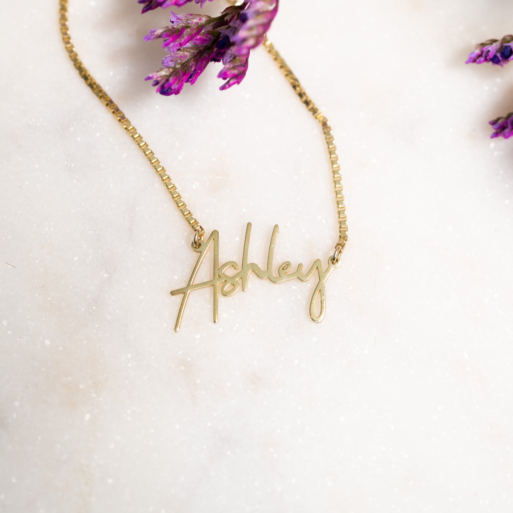 Flat lay wearing gold script custom name necklace with box chain