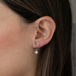 Model wearing a celestial earring stack including a sterling silver sunburst charm huggie and a lightning bolt stud.