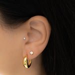 Model wearing chunky gold hoop earrings with solitaire stud diamond earrings