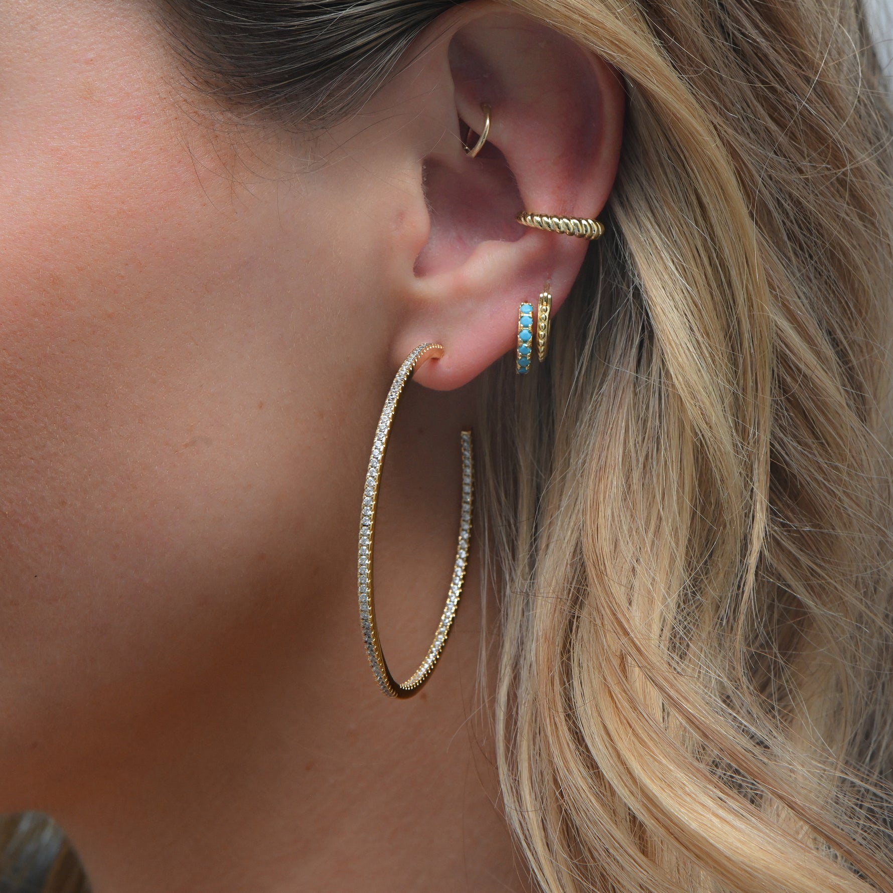 Model wearing large gold pave hoops with stacking huggies and gold croissant ear cuff