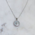 Silver mother of pearl cross circle pendant necklace on a marble background.
