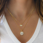 Model wearing dainty gold opal evil eye necklace paired with a mother of pearl cross pendant necklace.