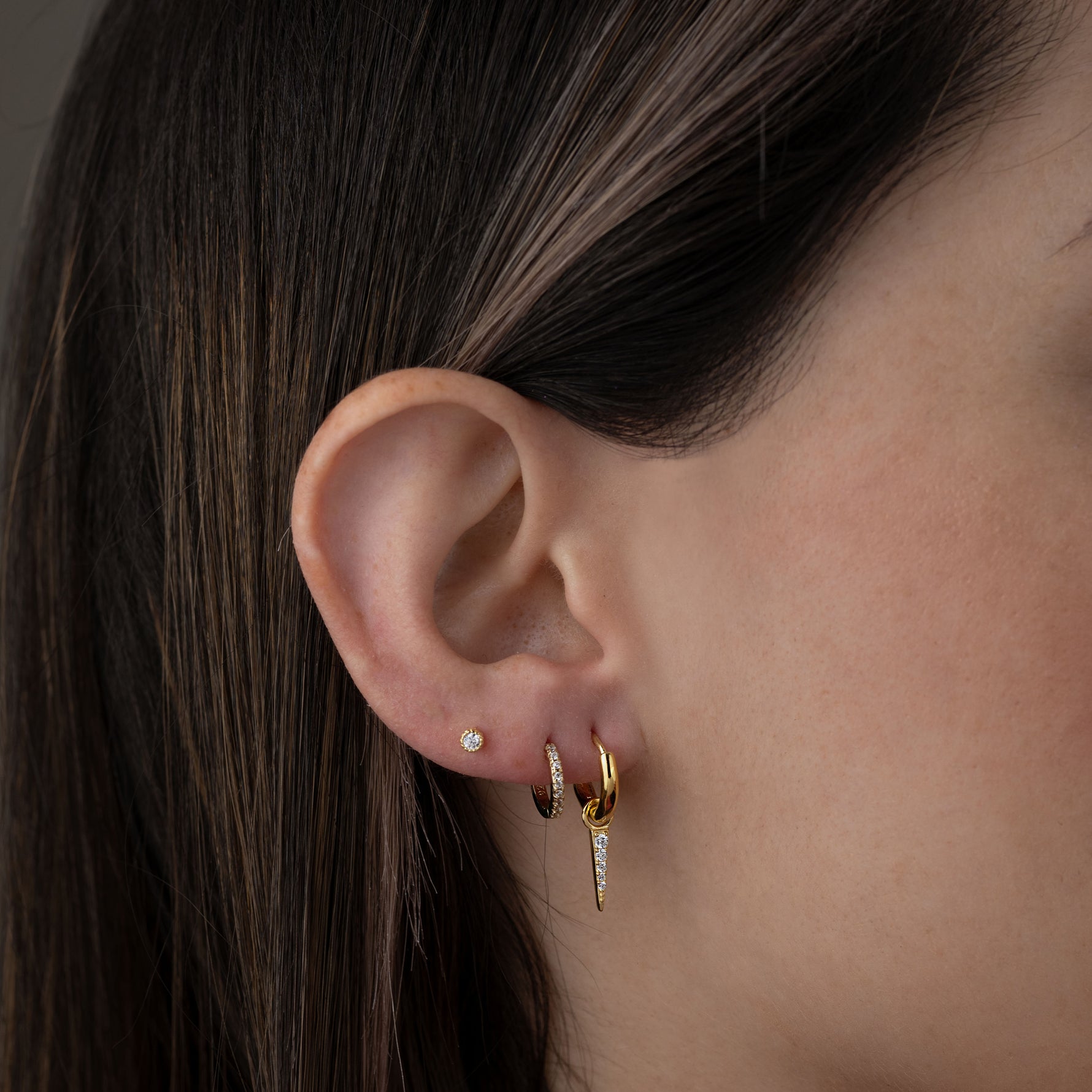 Model wearing small gold charm huggie earrings with spike charm paired with pave huggies and stud earrings