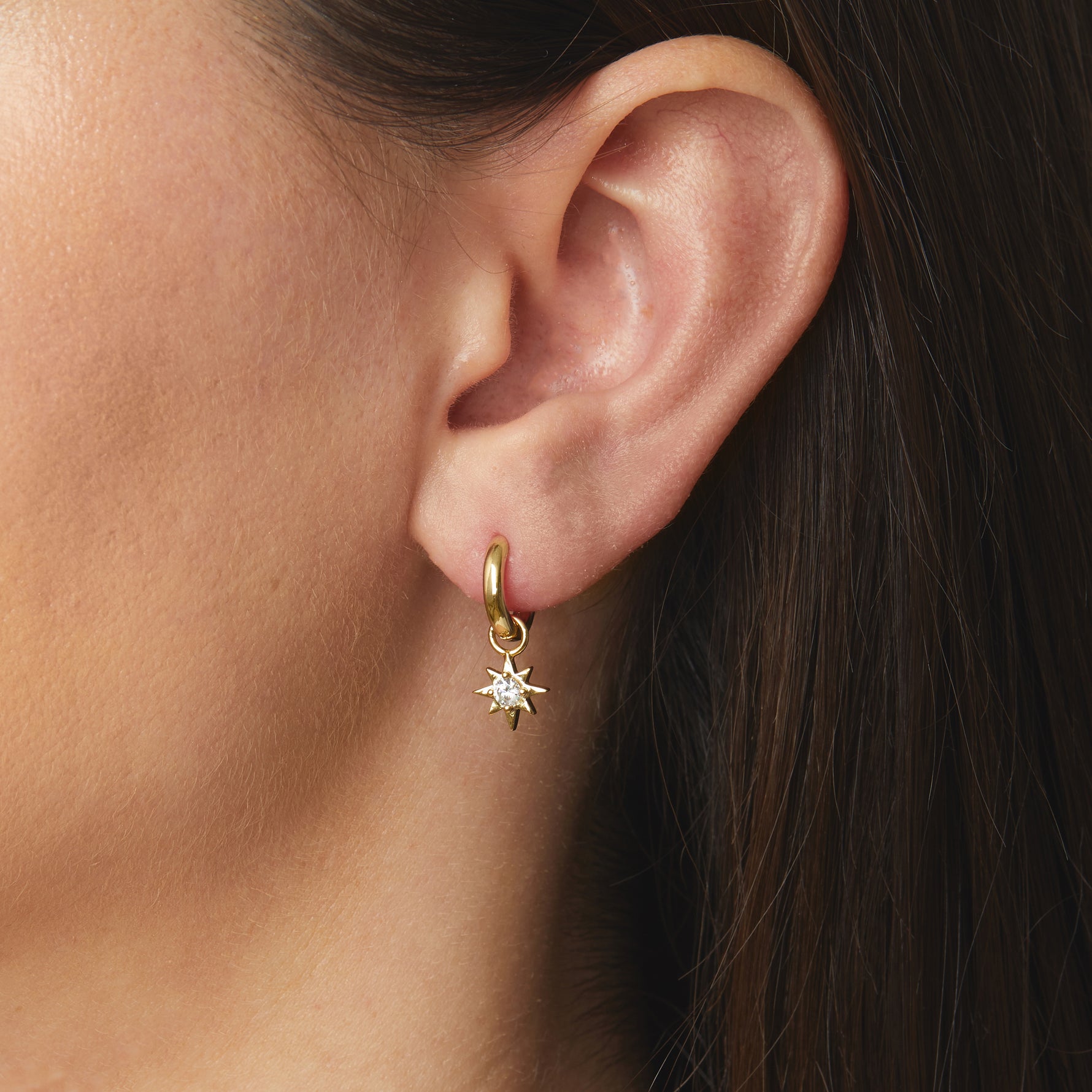 Model wearing minimalist gold charm huggie earrings with a sunburst charm.