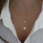 Model wearing trendy gold layered necklaces featuring a dainty chain necklace, a tiny bezel pendant necklace, and a sunburst medallion chain necklace.