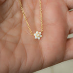 Model holding dainty gold opal flower pendant necklace.