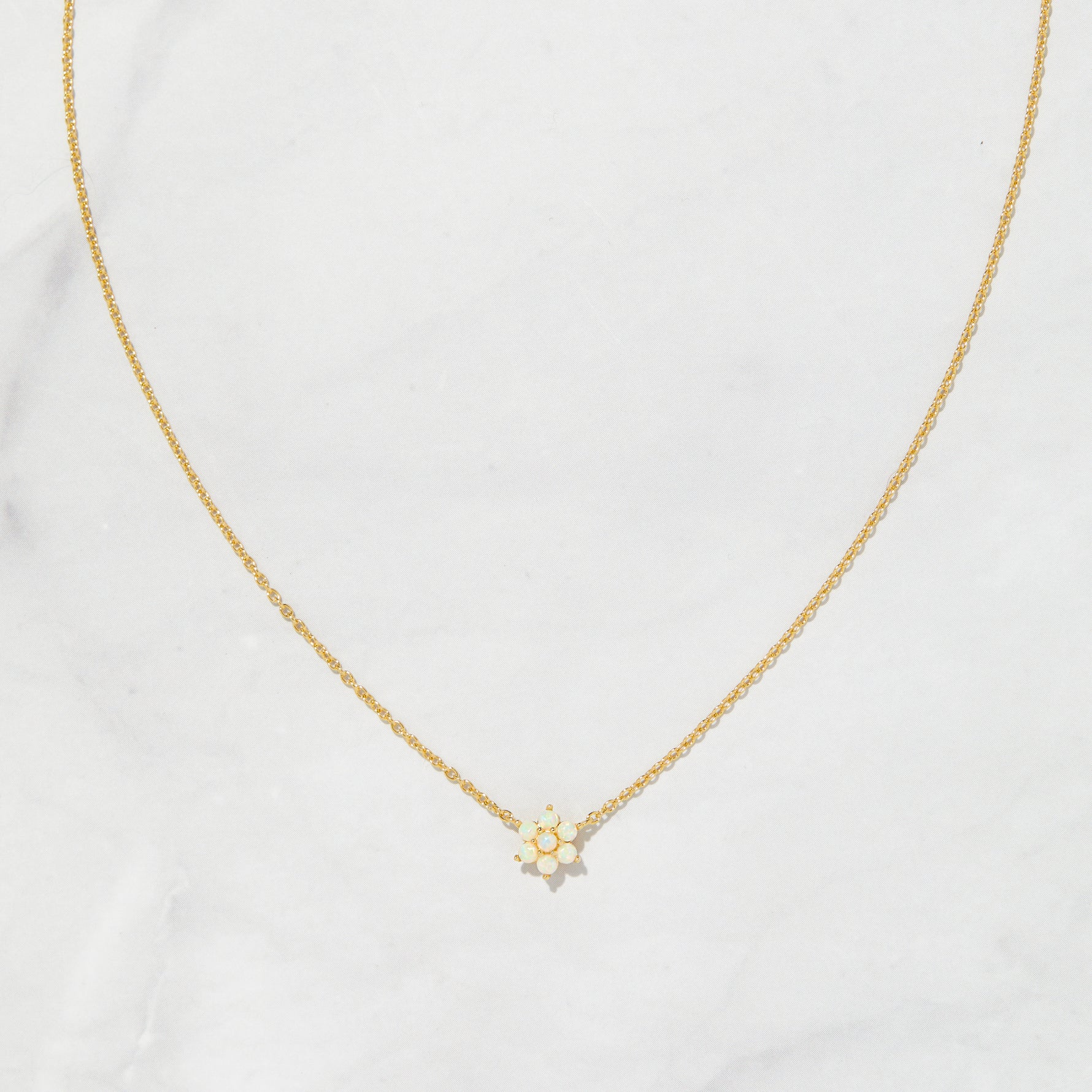 Opal flower necklace with delicate gold chain on marble background.