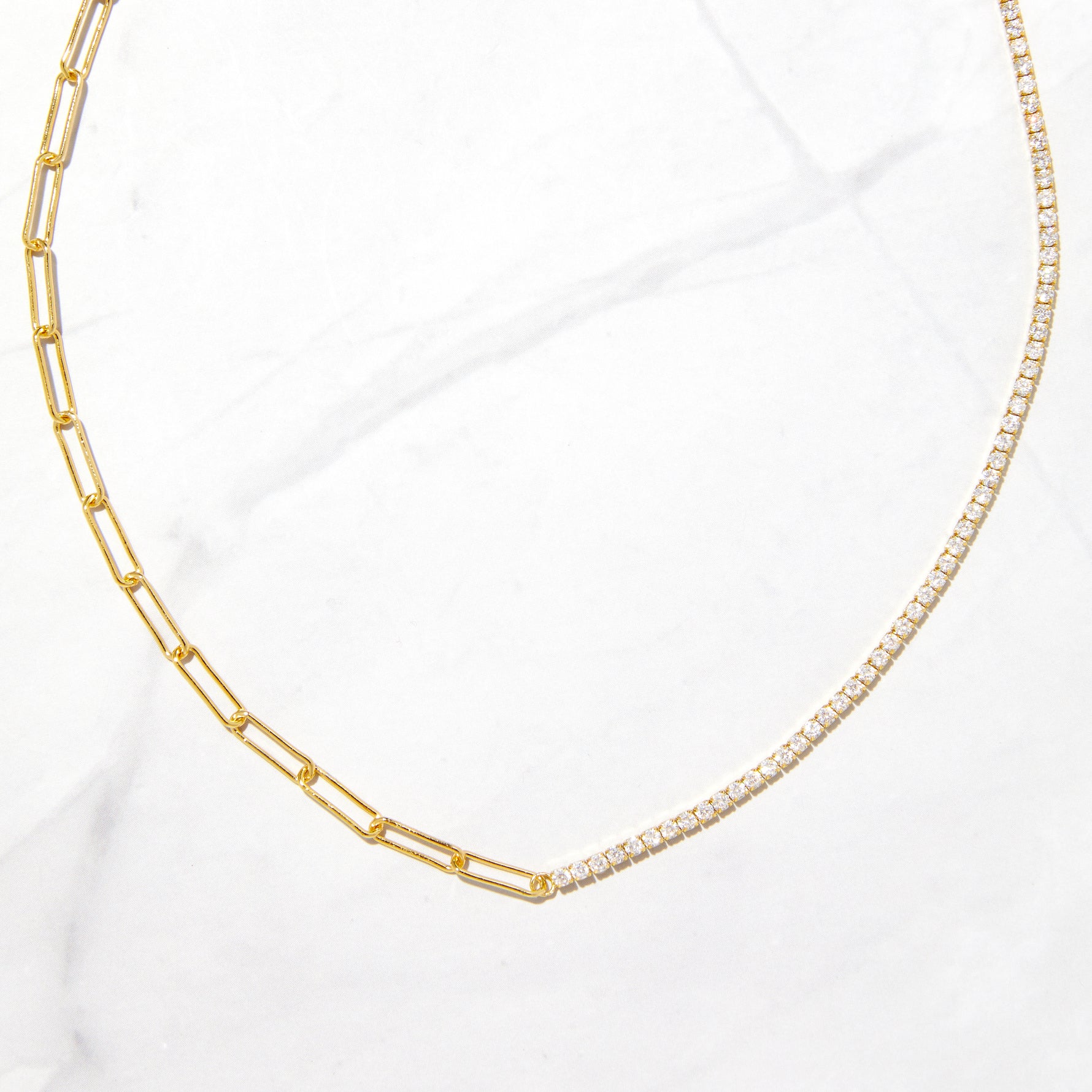 Gold half tennis and half paperclip necklace on marble background. 