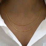 Model wearing two dainty gold chain necklaces featuring a thin twisted chain and a milla thin gold chain. 