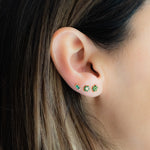 Model wearing solid emerald flower stud earrings, emerald flower studs with white cz center, and emerald baguette stud earrings in a stack.