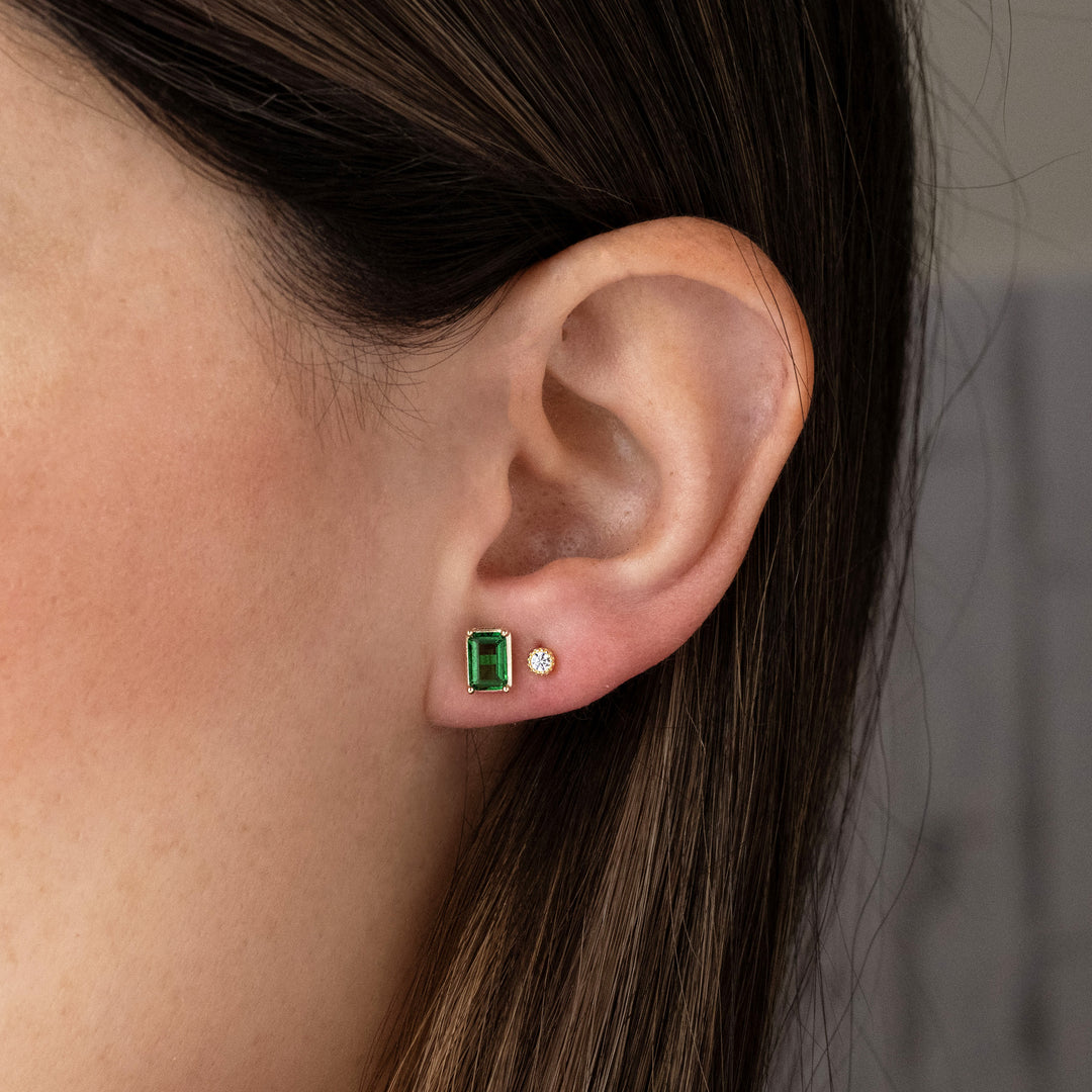 Model wearing emerald gold stud statement earrings paired with round bezel stud.