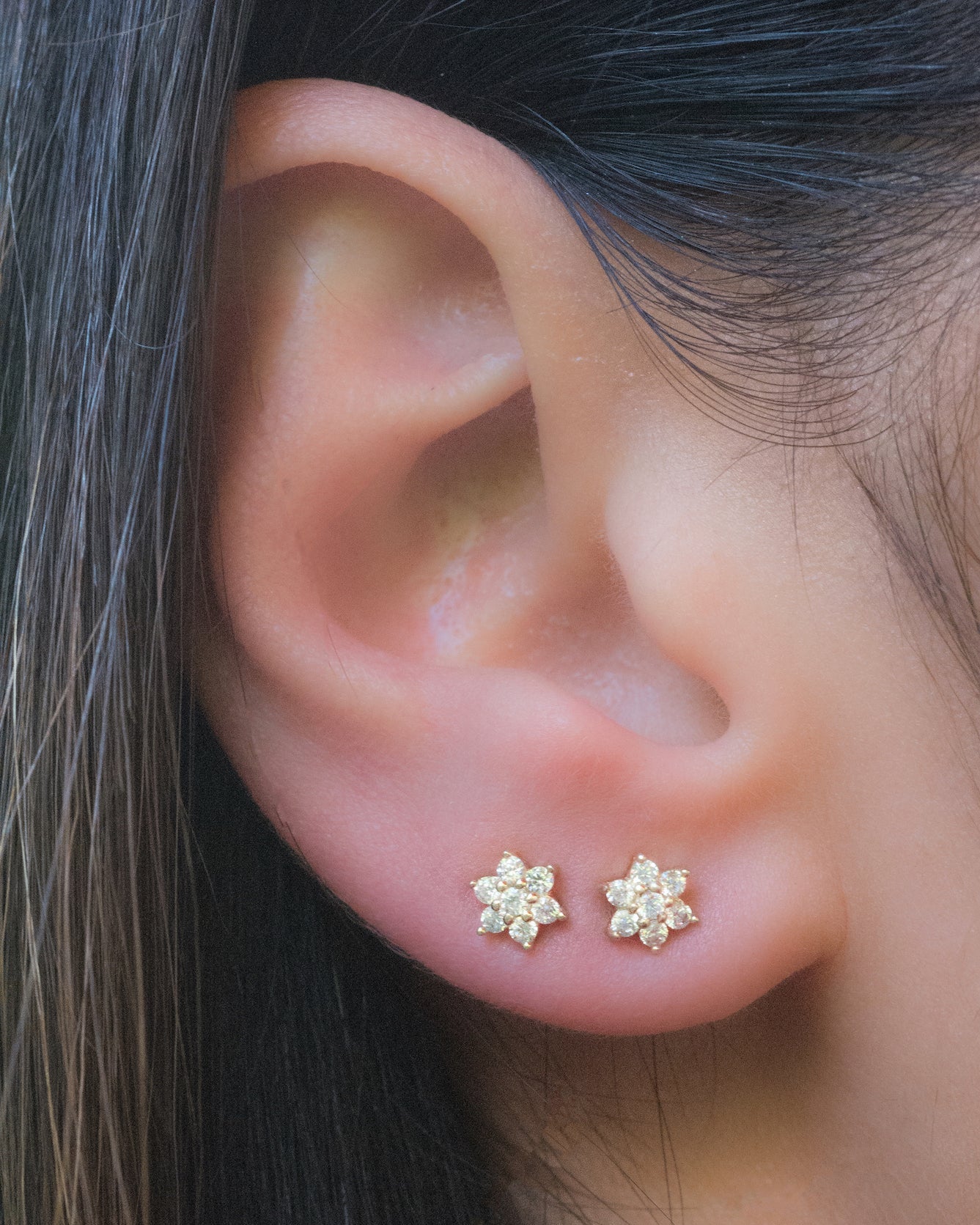 Model wearing two dainty gold cz flower stud earrings. 